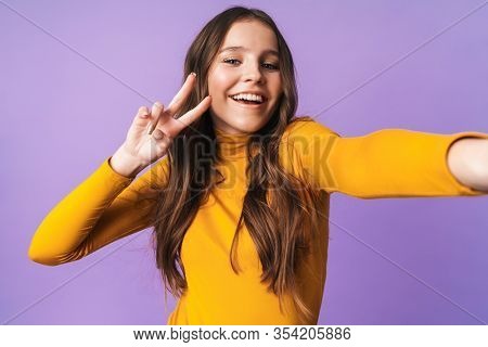 Image of young beautiful woman with long brown hair gesturing and taking selfie photo cellhone isolated over violet background