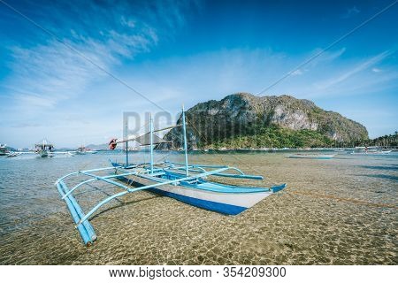 El Nido, Palawan, Philippines. Tourist Banca Boat On The Sandy Beach In Low Tide With Huge Rock Of C