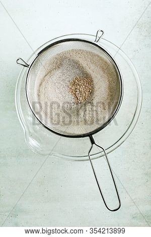 Sifting Flour Through A Sieve Into A Large Glass Bowl.