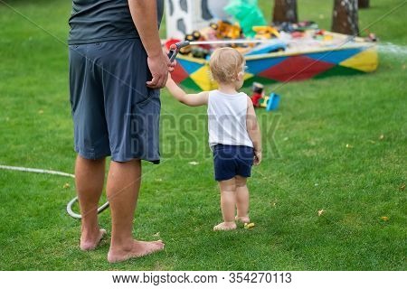 Father With Son Together Watering Garden And Green Grass Lawn At Home Backyard Outdoors On Brigh Sum