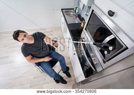 Disabled Man Using Grabber Tool To Control Microwave In Kitchen