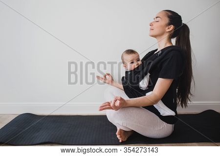 Young Mother Doing Yoga Exercises And Meditation With Her Little Baby In Ergo Backpack.