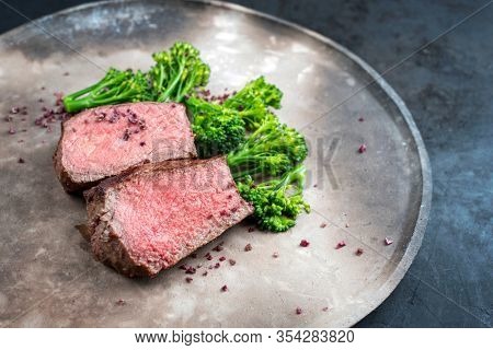 Barbecue dry aged wagyu roast beef natural sliced offered with rapini and salt as closeup on a modern design plate with copy space right