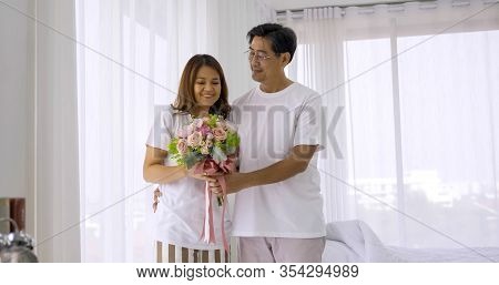 Happy Woman Receiving Flower Bouquet From Her Husband In The Room.