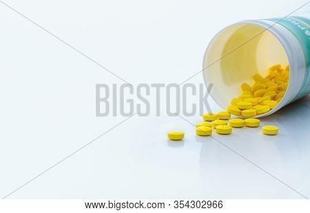 Yellow Tablets Pills Spread Out Of Drug Bottle. Tablets Pills With Bottle On White Table. Drug Produ