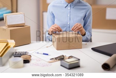 delivery, mail service, people and shipment concept - close up of woman packing parcel box and tying rope at post office