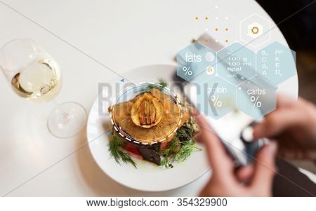 food, technology, eating and people concept - woman with smartphone, breaded fish fillet and nutritional value chart at restaurant