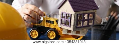 Close-up Of Male Hands Driving Toy Excavator On Building. Businessman At Workplace With Big Blueprin