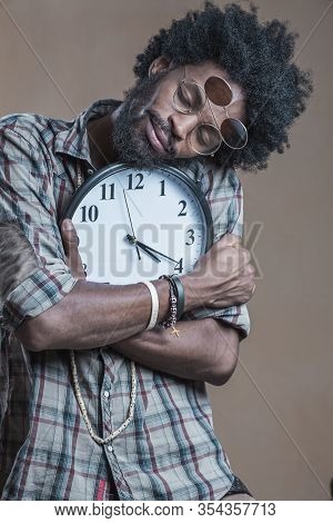 A Curly-haired Dominican With Open Glasses On His Glasses Embraces A Large Wall Clock And Smiles