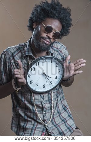 A Curly-haired Dominican With Open Glasses On His Glasses Embraces A Large Wall Clock And Smiles