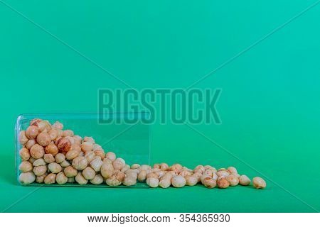 Plastic Container Tilted On A Surface With Macadamias Watered With A Green Background, Also Called Q