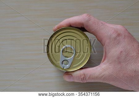 Hand Of An Adult Man Holds A Can Of Canned Food. Closed Tin Can With Open Key In Hand. A Mans Hand H