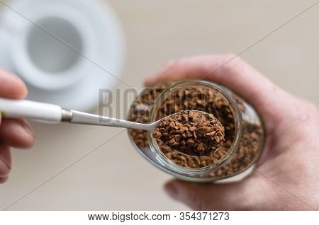 Glass Jar With Coffee In A Hand. A Hand Holds A Spoon Full Of Instant Coffee. Pile Of Instant Coffee