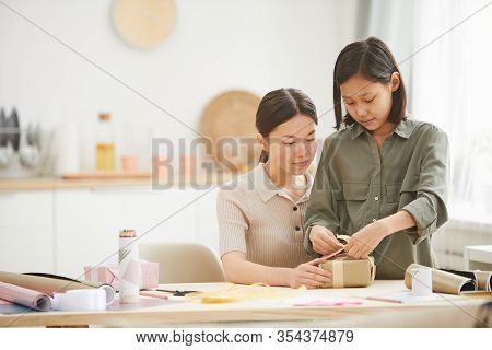 Young Asian Woman And Teen Girl Spending Time Together At Hme Preparing Gifts For Mothers Day Holida