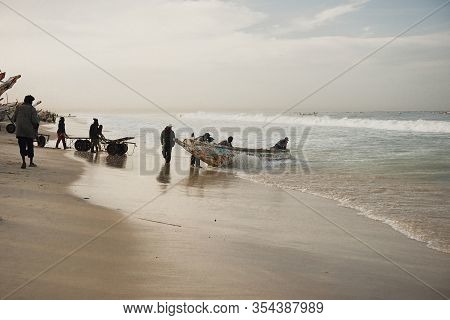 Kayar, Senegal - January 17, 2020: Fishermans Pushing Traditional Painted Wooden Fishing Boat In Kay
