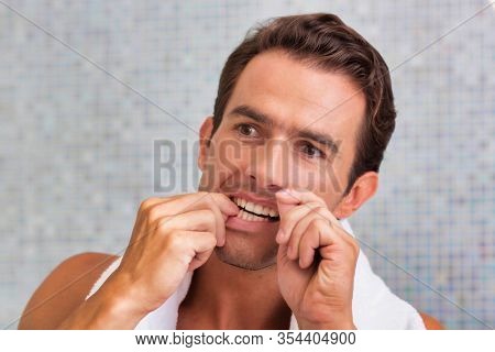Portrait of attractive man looking in the mirror while flossing hsi teeth 