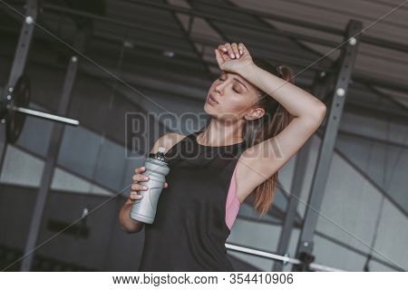 Portrait Of Tired Young Fitness Woman Holding Shaker With Water In Hand And Relaxing While Standing 