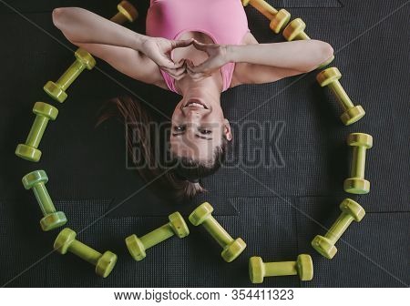 Top View Happy Young Fitness Woman In Sports Wear Laying On Floor And Showing Heart Shape By Hands W