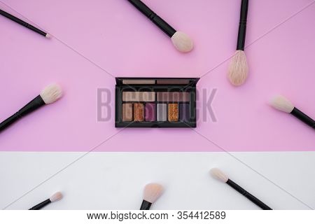 Side View Of Colorful Metallized Eyeshadow Pallete And Natural Makeup Brushes Set On White And Pink 