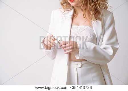 Elegant Curly Lady In White Suit And Lace Bra Holds Wireless Headphones In Her Hands Isolated Over W