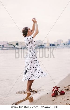 Cheerful Young Woman In White Polka Dot Dress Holding Hands Up And Smiling, Have Fun And Turn Around