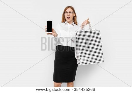Image Of A Young Pregnant Businesswoman Wearing Glasses, Shows A Blank Smartphone Screen, With Packa