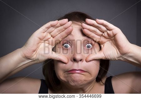 Woman Grimaces In Front Of Camera On Gray Background