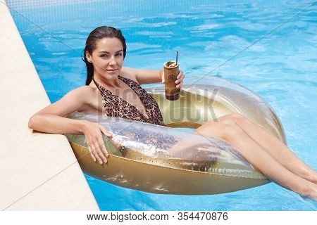 Outdoor Shot Of Young Brunette Woman With Wet Hair Relaxing On Inflatable Swim Ring, Wearing Fashion