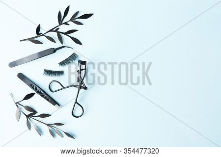 False Lashes With Black Tweezers And Paper Leaves On Blue Background With Copy Space