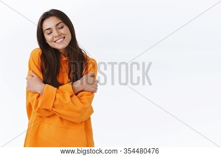 Tenderness And Women Concept. Adorable Caucasian Female Brunette In Orange Hoodie, Close Eyes And Sm