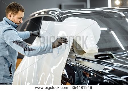 Man Preparing Protective Film For Sticking On A Car Body, Taking It From The Roll At The Vehicle Ser