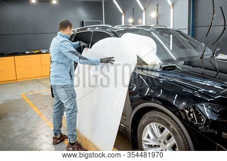 Man Preparing Protective Film For Sticking On A Car Body, Taking It From The Roll At The Vehicle Ser