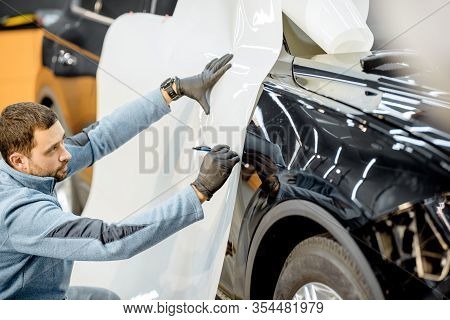 Man Preparing Protective Film For Sticking On A Car Body, Marking It To With A Pen At The Vehicle Se