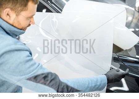 Man Preparing Protective Film For Sticking On A Car Body, Marking It To With A Pen At The Vehicle Se