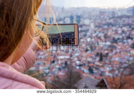 Girl With Glasess And Brown Hair Photographing Sarajevo With Mobile Phone