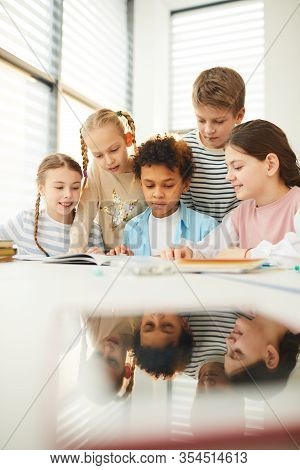 Group Of Modern Classmates Helping Their Good Friend With Homework Task He Couldnt Do, Vertical Shot