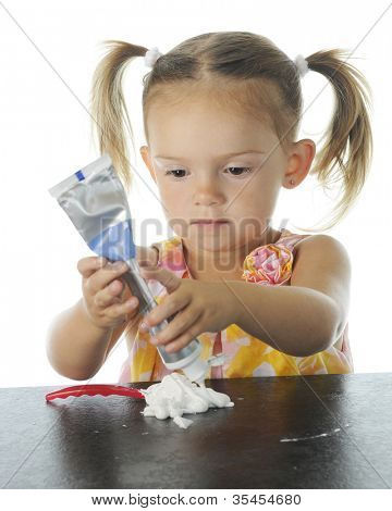 Rozkošný preschooler soustředí na mačkání zubní pasta na její zubní kartáček.  Zaměřit se na dítě 