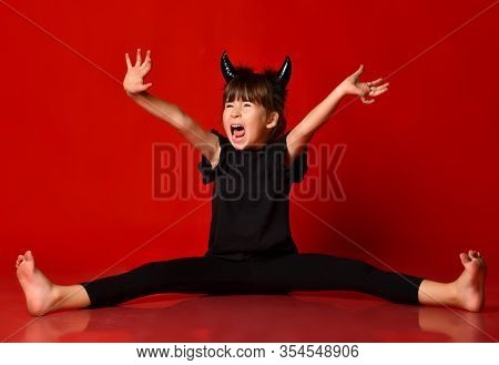 Little Brunette Kid With Devil Horns, In Black Blouse And Leggings, Barefoot. She Is Screaming While