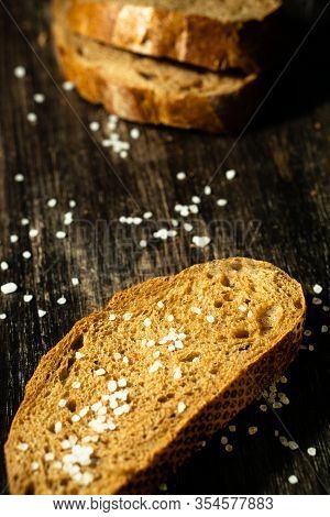 Fresh Slice Of Dark Bread With Salt On A Wooden Surface. Healthy Food With Rye Flour Or Yeast.