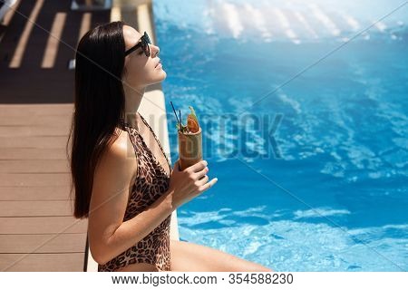 Profile Of Dreaming Cute Sweet Female Sunbathing, Sitting Near Swimming Pool, Holding Cocktail, Bein