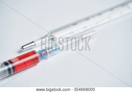 Syringe With Medicine Red For Lowering Temperature Next To A Thermometer On A White Background. Clos