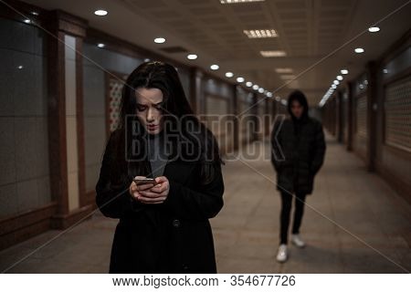 A Young Beautiful Woman Walks Through An Underground Passage At Night, Followed By A Man In Dark Clo