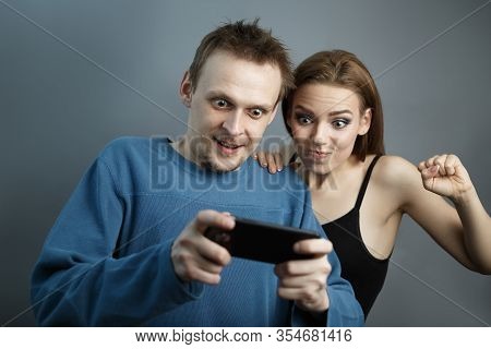 Man With The Girl Excitedly Looking At The Smartphone On Gray Isolated Background. Concept Of Playin