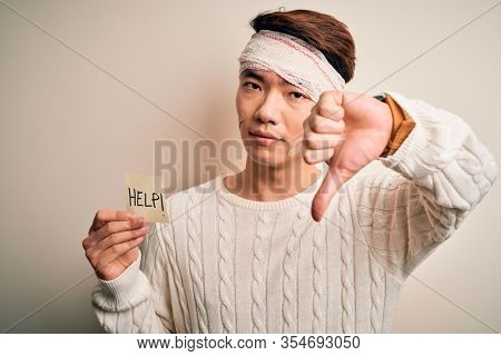 Young handsome chinese man injured for accident wearing bandage on head asking for help with angry face, negative sign showing dislike with thumbs down, rejection concept