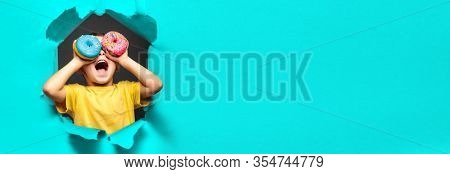 Happy cute boy is having fun played with donuts on black background wall. Bright photo of a boy. Colored donuts. panorama