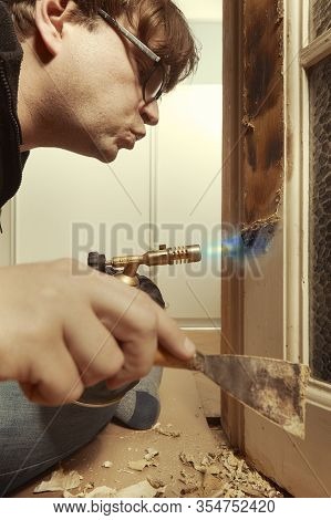 Man At Home Removing Havy Layer Of Old Paint From Door With Burner