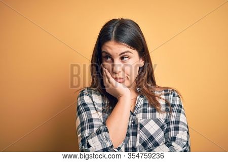 Young beautiful woman wearing casual shirt standing over isolated orange background thinking looking tired and bored with depression problems with crossed arms.