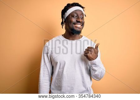 Young african american man doing sport wearing sportswer over isolated yellow background smiling with happy face looking and pointing to the side with thumb up.