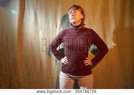 A Middle-aged Woman Poses Showing Clothes Against A Background Of Green Crumpled Curtains. An Inept 