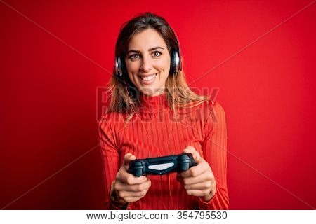 Young beautiful brunette gamer woman playing video game using joystic and headphones with a happy face standing and smiling with a confident smile showing teeth